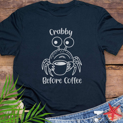 Navy blue t-shirt with a crab graphic and text 'Crabby Before Coffee' on a wooden surface.