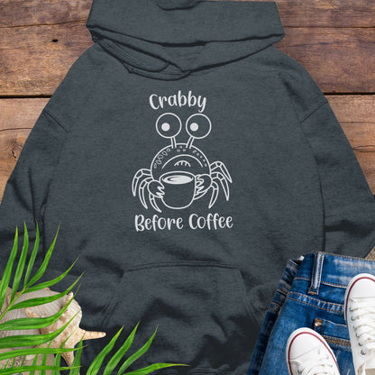 Dark gray hoodie with a crab graphic and text 'Crabby Before Coffee' on a wooden surface.