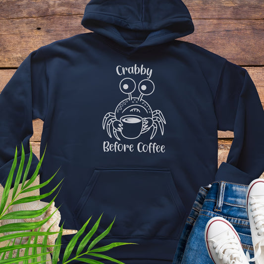 Navy blue hoodie with a crab graphic and text 'Crabby Before Coffee' on a wooden surface.