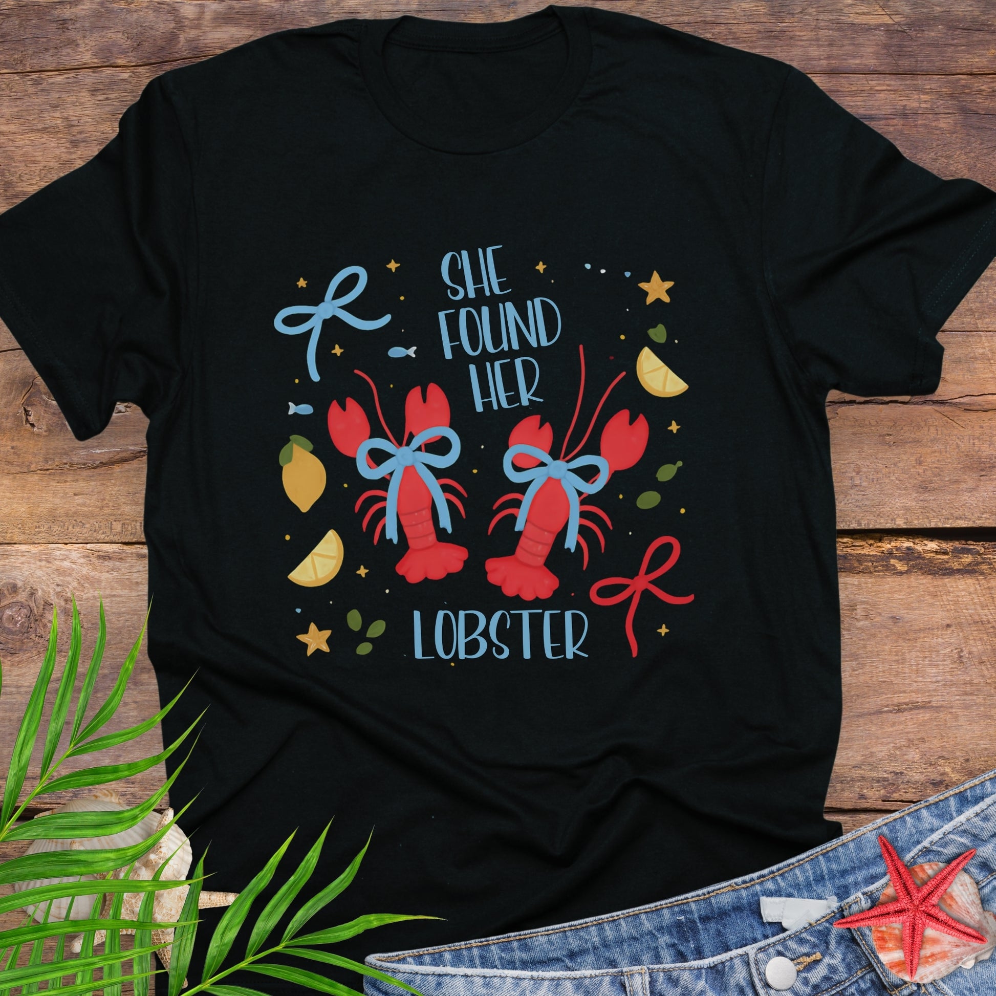 Black T-shirt with two lobsters and blue bows that says She Found Her Lobster.