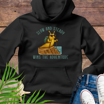 Black hoodie with a graphic of a snail and text 'Slow and Steady Wins the Adventure' on a wooden background.