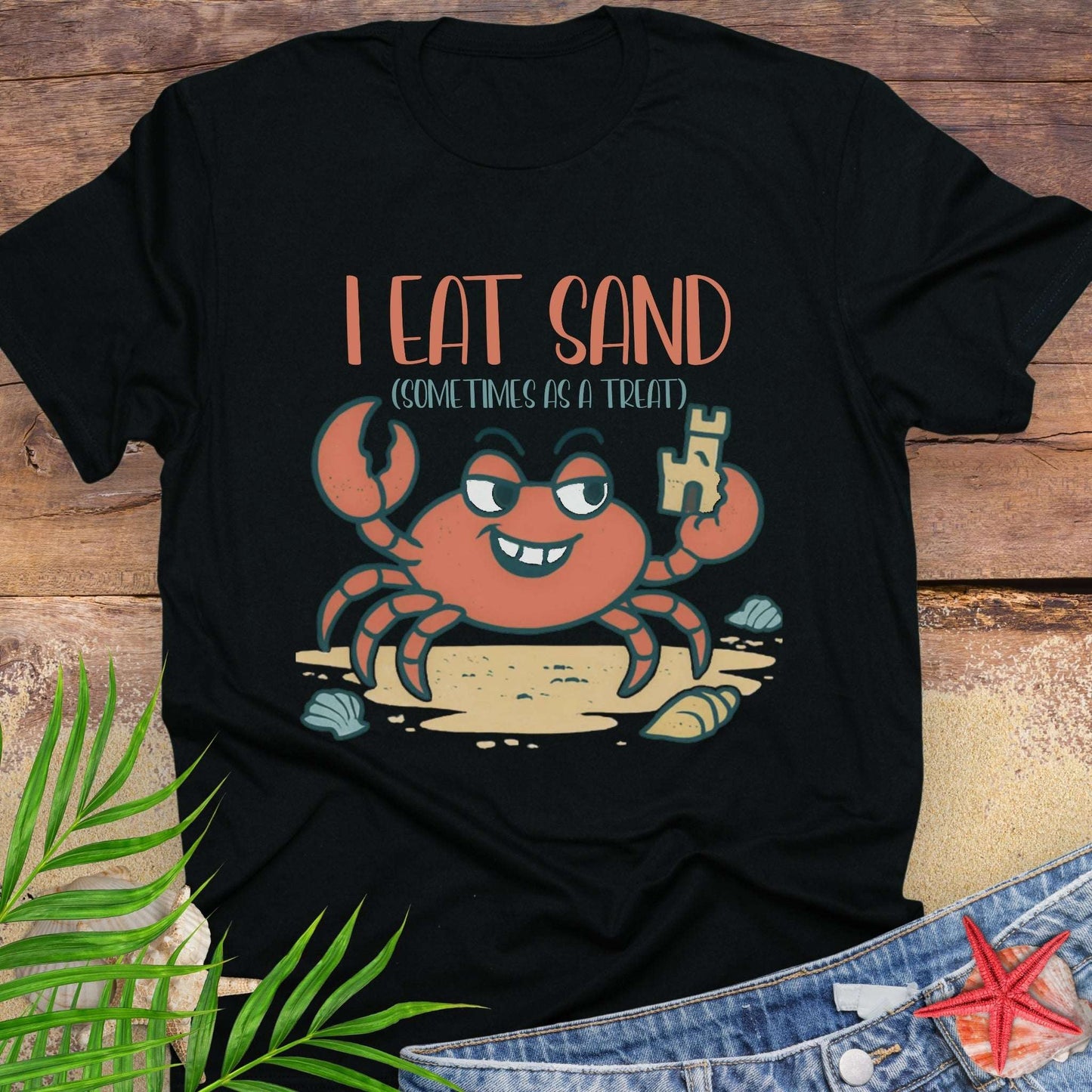 Black t-shirt with a cartoon crab design and text on a wooden surface.