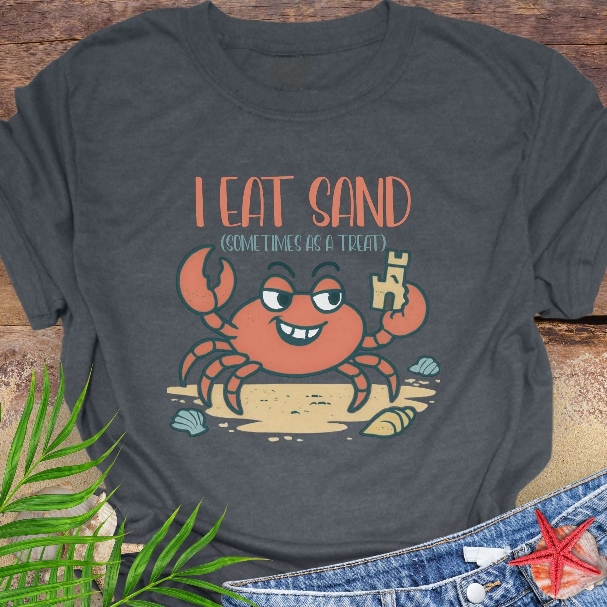 Gray t-shirt with a cartoon crab and text 'I eat sand sometimes as a treat' on a wooden surface.