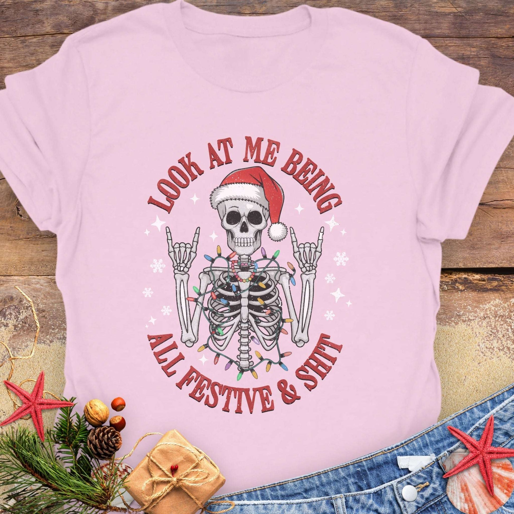 Pink t-shirt with skeleton wearing a Santa hat and lights wrapped around body design and text 'Look at me being all festive and shit.