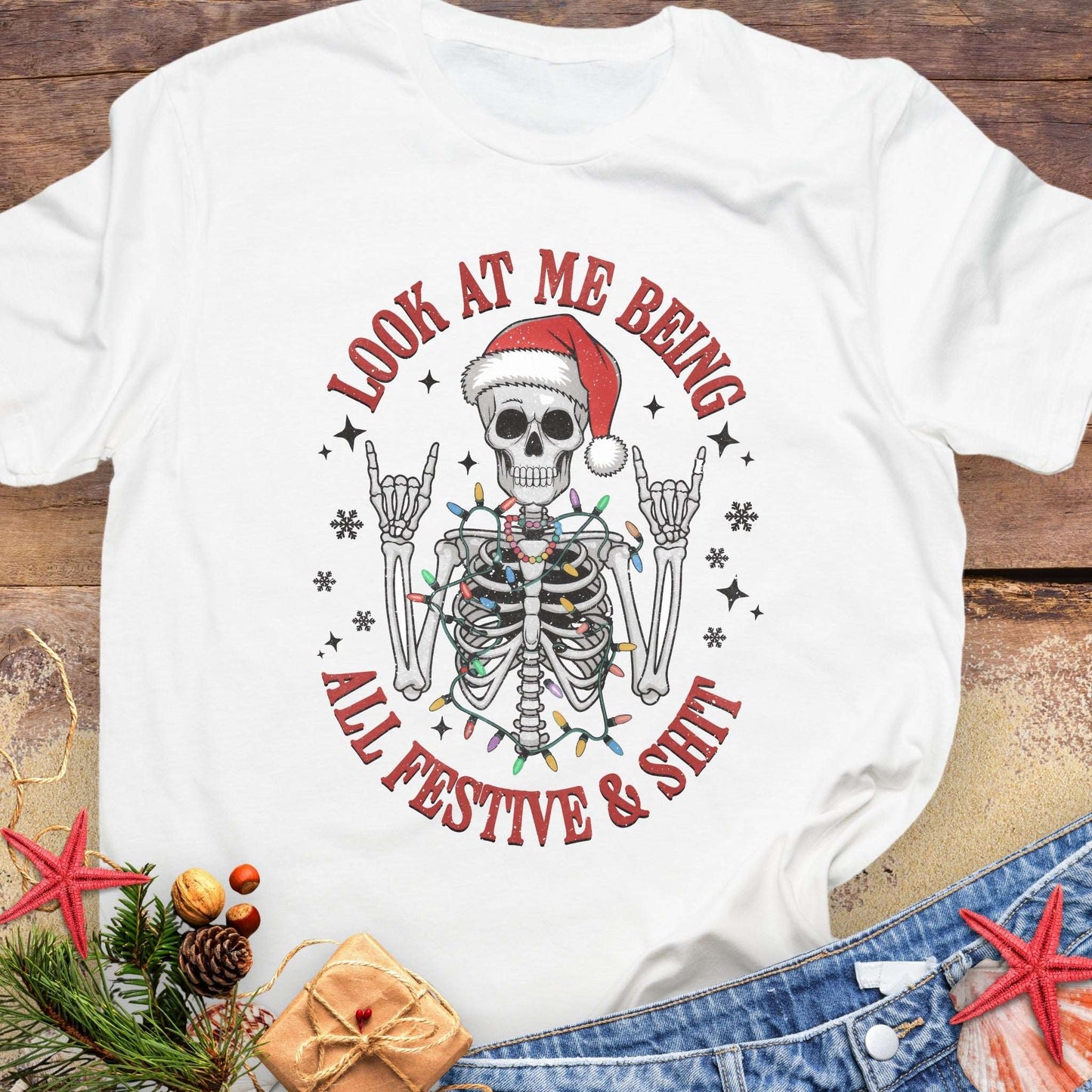 White t-shirt with skeleton wearing a Santa hat and lights wrapped around body design and text 'Look at me being all festive and shit.