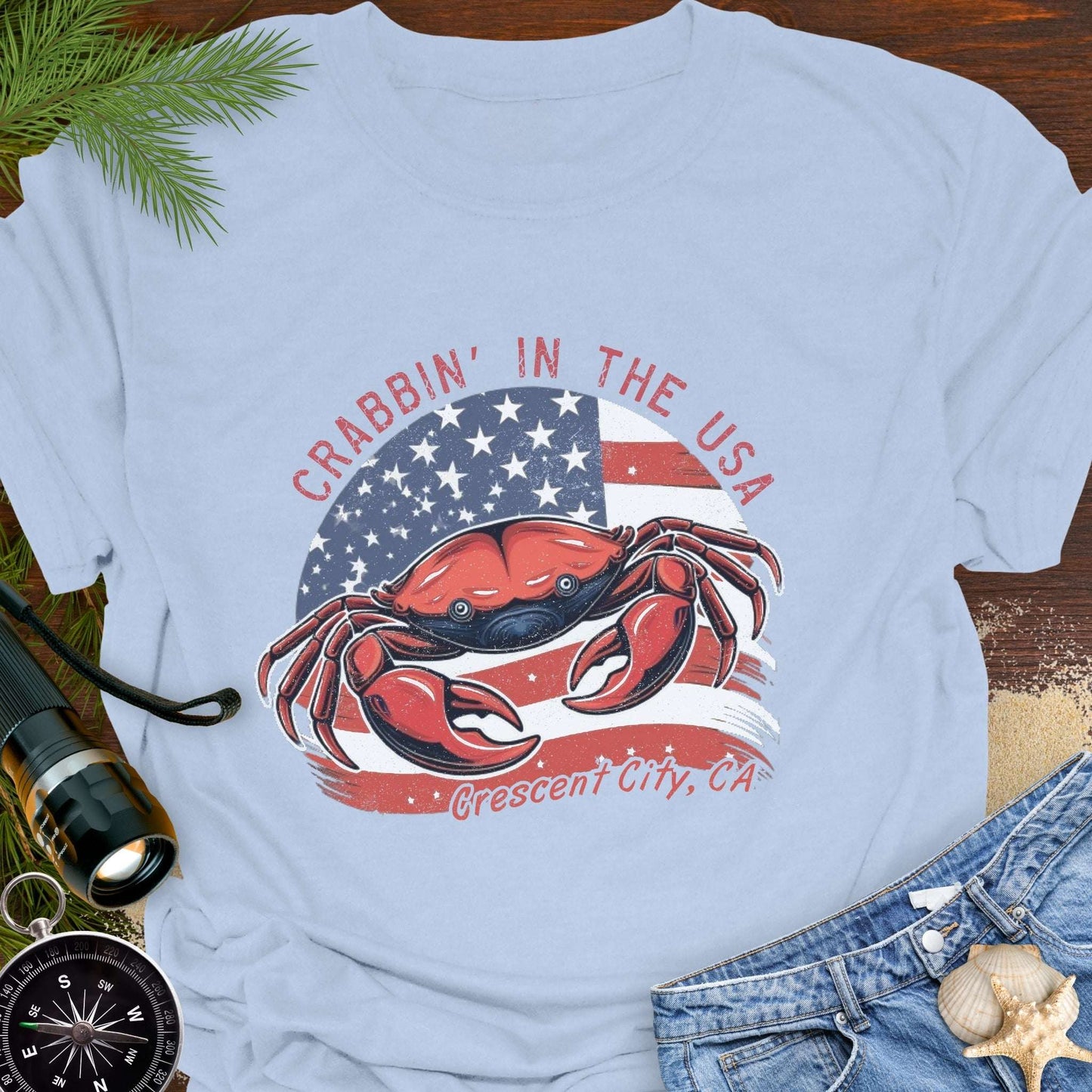 Light blue t-shirt with a crab and American flag design and text 'Crabbin' in the USA – Crescent City, CA'. 