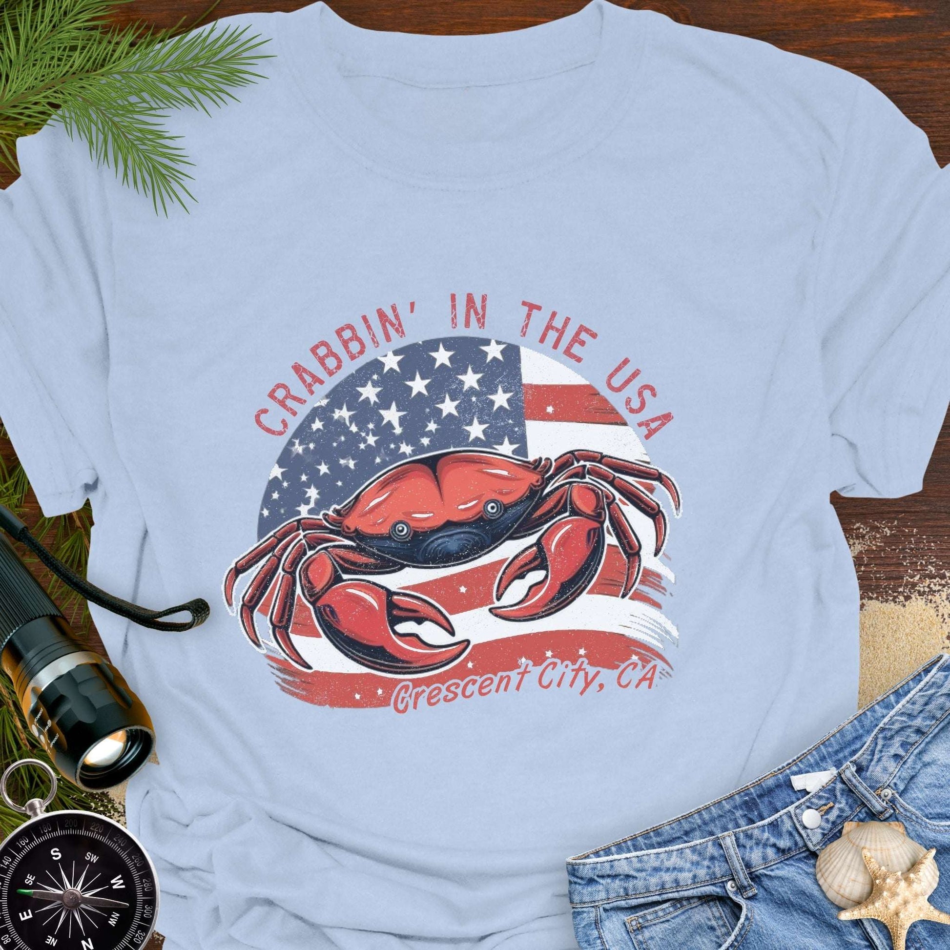 Light blue t-shirt with a crab and American flag design and text 'Crabbin' in the USA – Crescent City, CA'. 