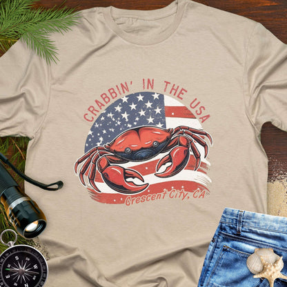 Beige t-shirt with a crab and American flag design and text 'Crabbin' in the USA – Crescent City, CA'. 