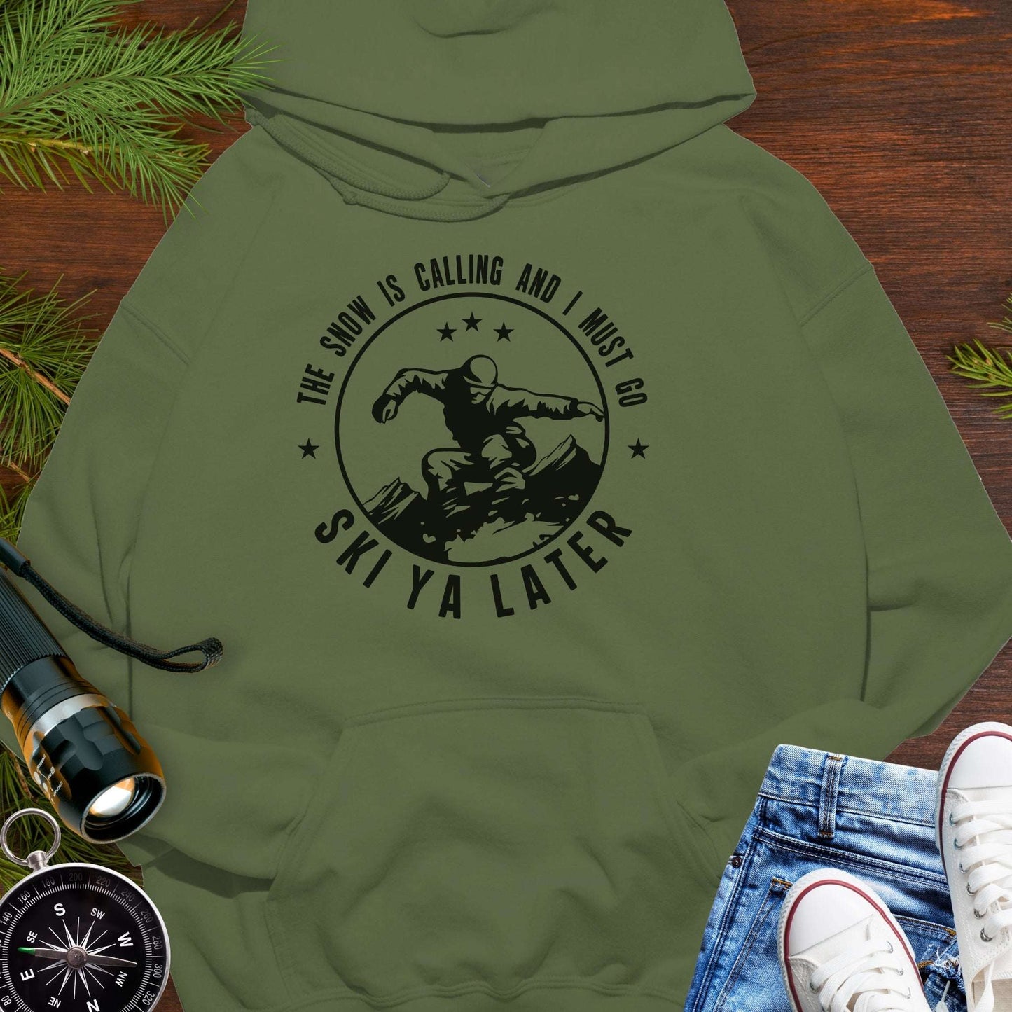 Military Green hoodie with skiing graphic and text 'The snow is calling and I must go Ski Ya Later'.