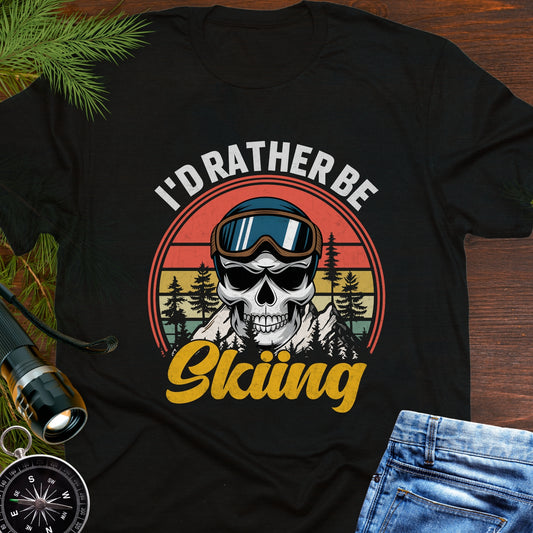 Black T-shirt graphic showing a skeleton head wearing ski goggles in front of a retro sunset with mountains and trees, with text that reads “I’d Rather Be Skiing.