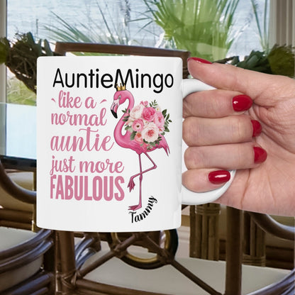 Mug with flamingo design and text held by a hand with red nails, outdoor setting.