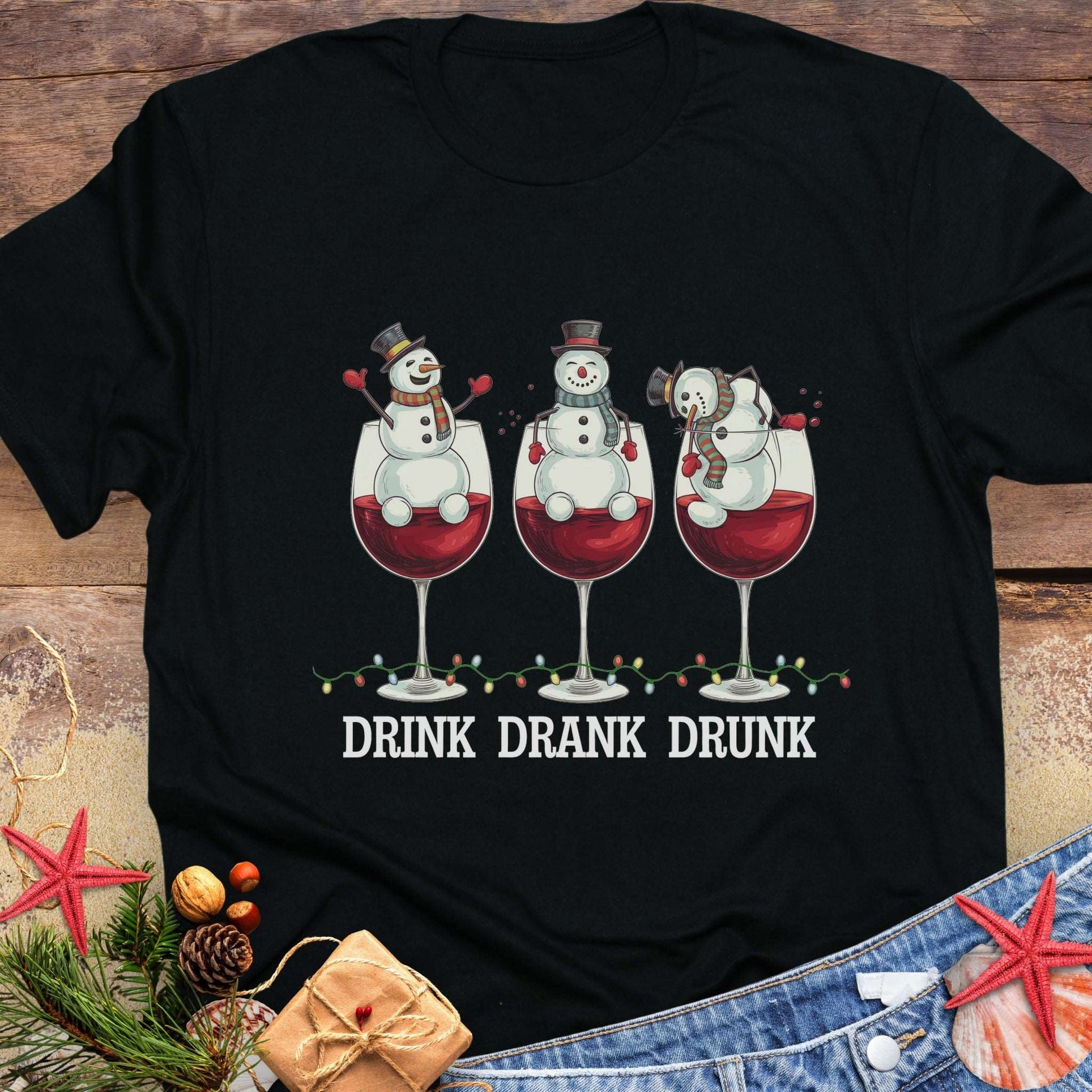 Black T-shirt with three snowmen sitting inside large wine glasses, raising smaller glasses above the text “DRINK DRANK DRUNK.