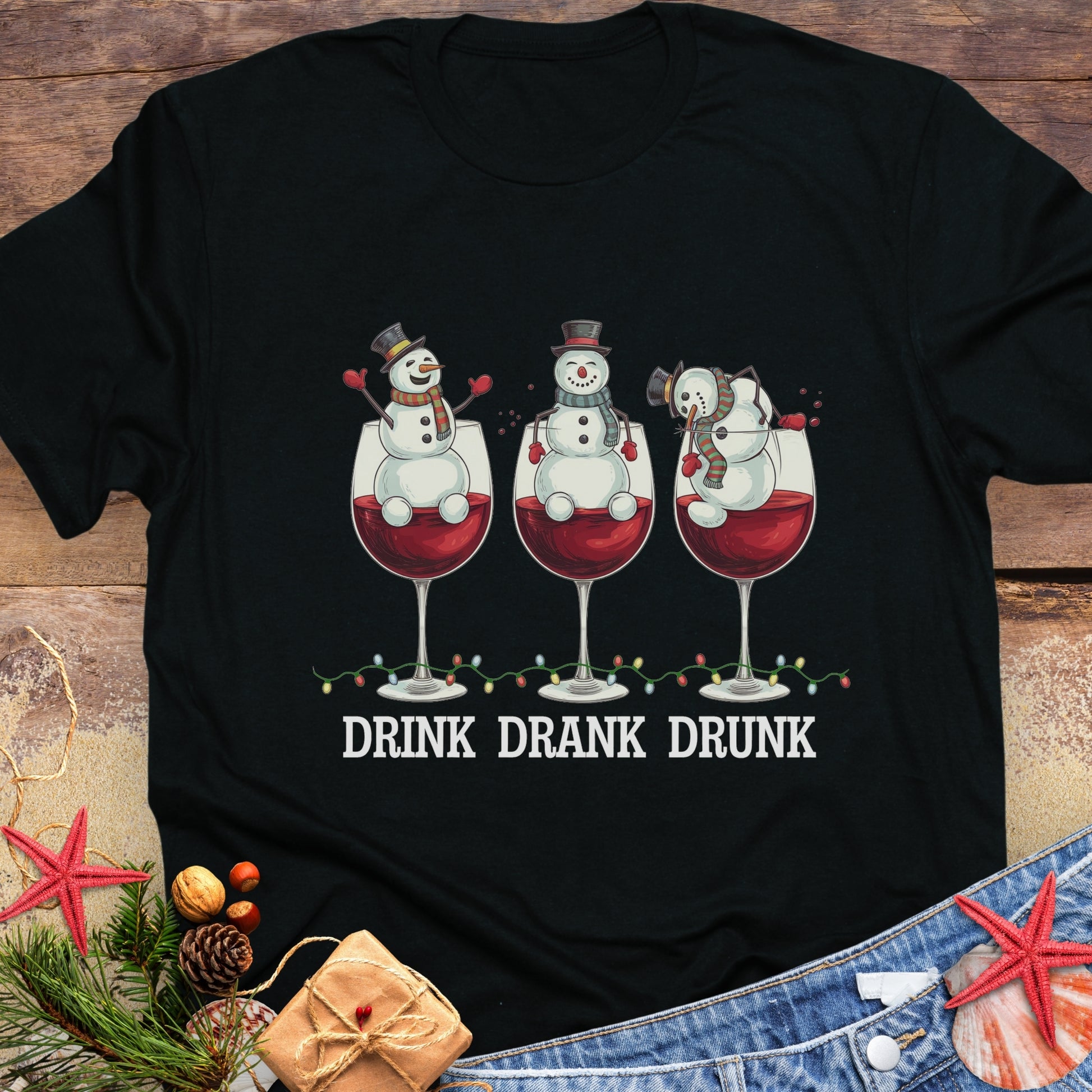Black T-shirt with three snowmen sitting inside large wine glasses, raising smaller glasses above the text “DRINK DRANK DRUNK.