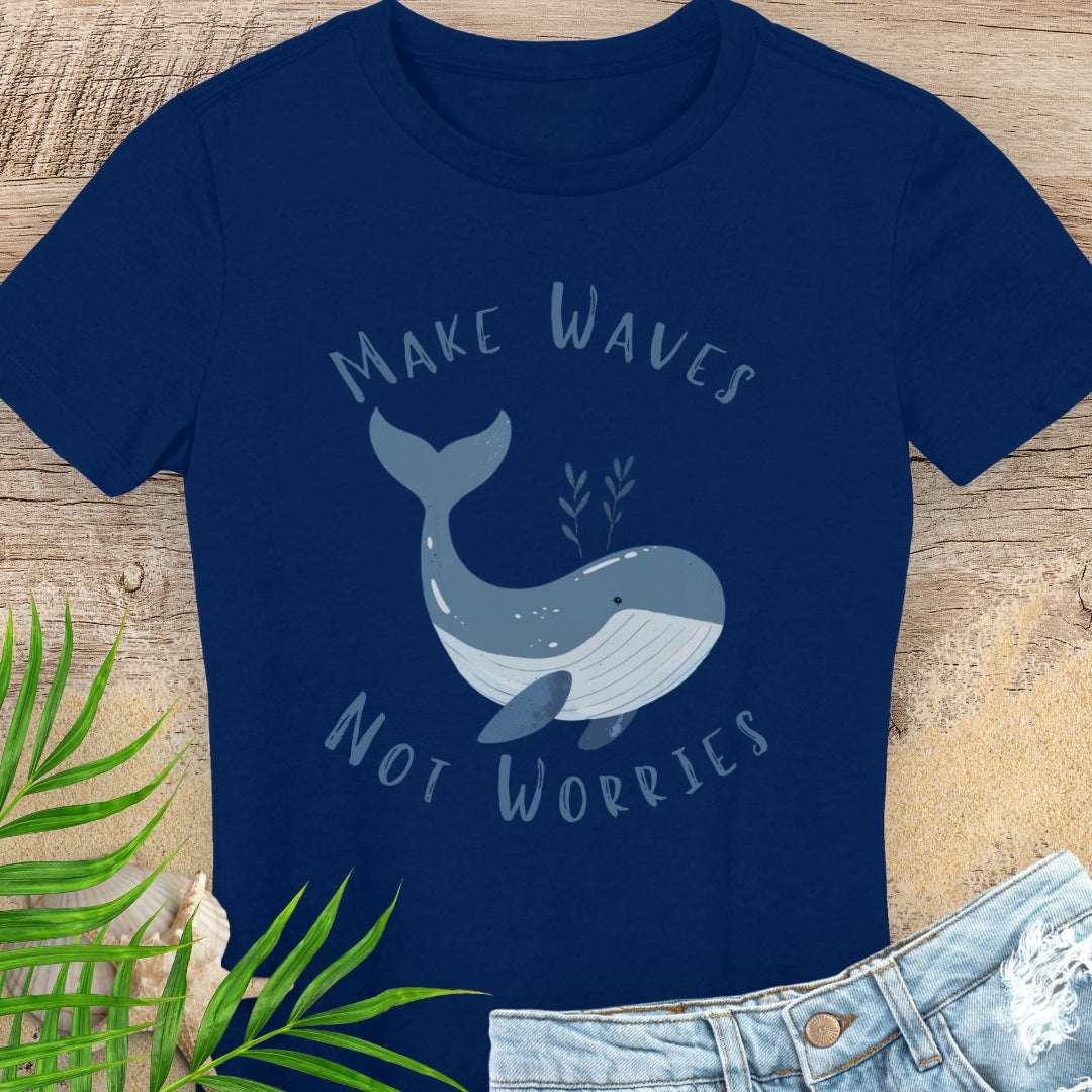 Navy blue t-shirt with a whale graphic and text 'Make Waves Not Worries' on a wooden surface.