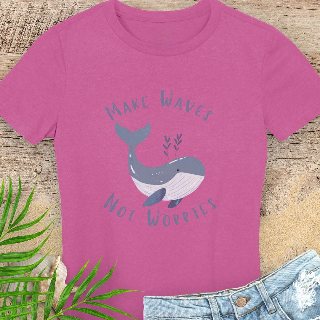 Pink t-shirt with whale graphic and text 'Make Waves Not Worries' on a wooden surface with leaves and jeans.