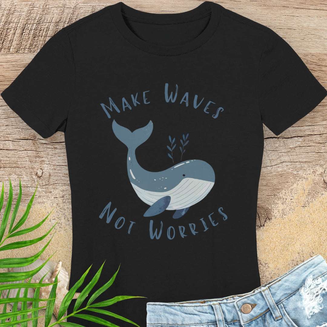 Black t-shirt with a whale graphic and text 'Make Waves Not Worries' on a wooden surface.