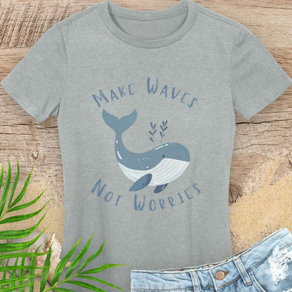 Gray t-shirt with whale design and text 'Make Waves Not Worries' on a wooden surface with leaves and jeans.