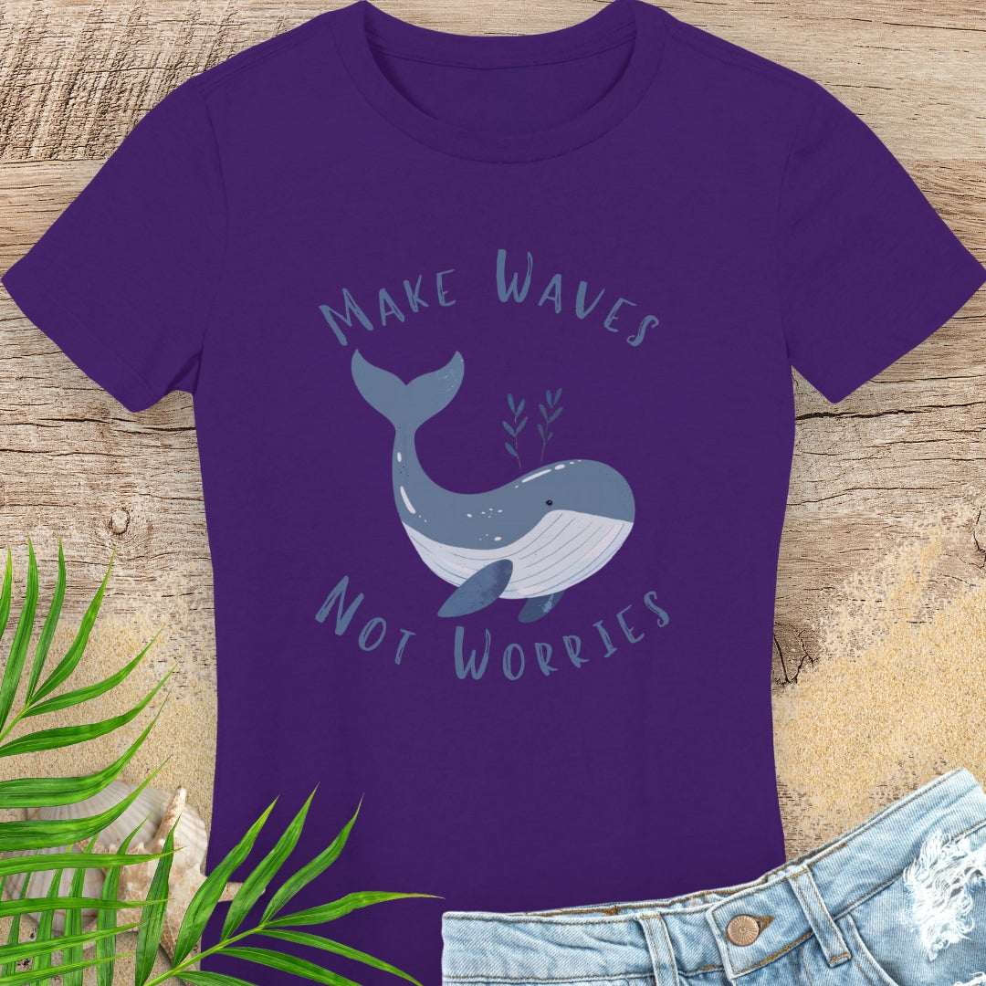 Purple t-shirt with a whale graphic and text 'Make Waves Not Worries' on a wooden surface with leaves and jeans.