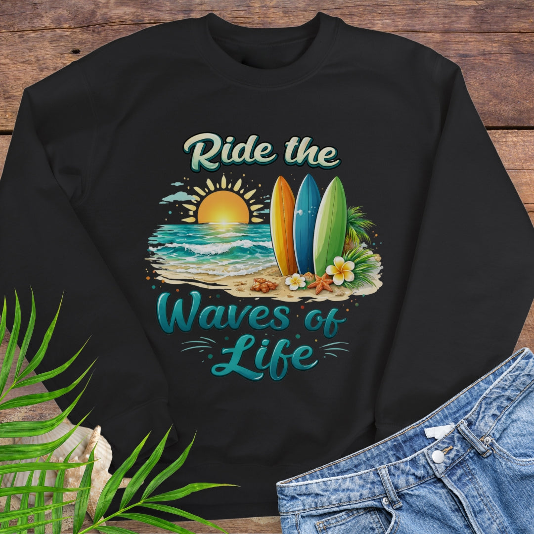 Black crewneck sweatshirt with inspirational Ride the Waves of Life beach design, showing surfboards, ocean sunset, palm leaves, and sand.