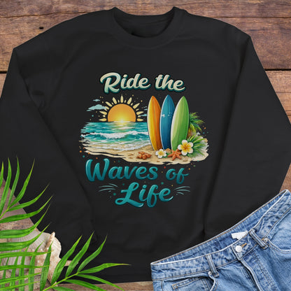 Black crewneck sweatshirt with inspirational Ride the Waves of Life beach design, showing surfboards, ocean sunset, palm leaves, and sand.