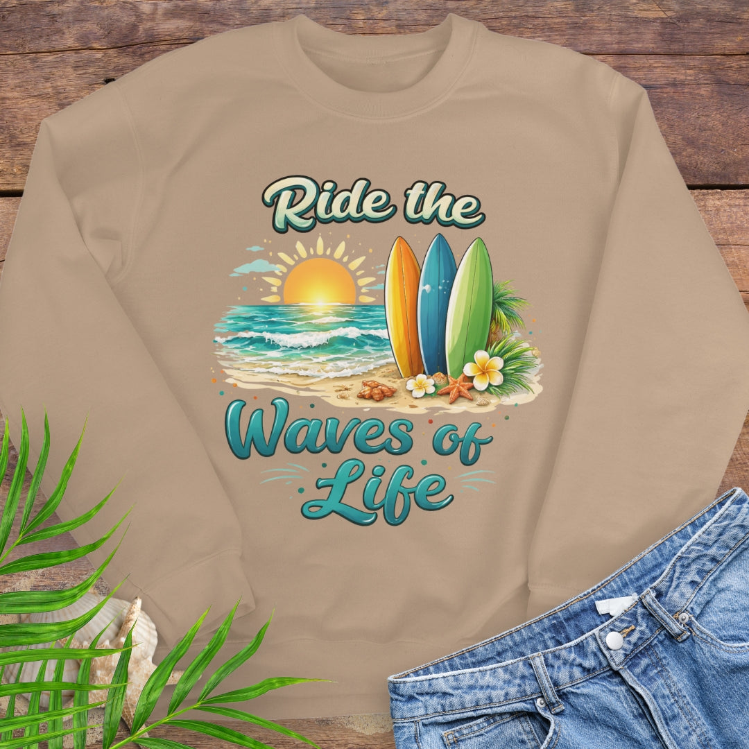 Beige crewneck sweatshirt with inspirational Ride the Waves of Life beach design, showing surfboards, ocean sunset, palm leaves, and sand.
