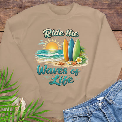 Beige crewneck sweatshirt with inspirational Ride the Waves of Life beach design, showing surfboards, ocean sunset, palm leaves, and sand.