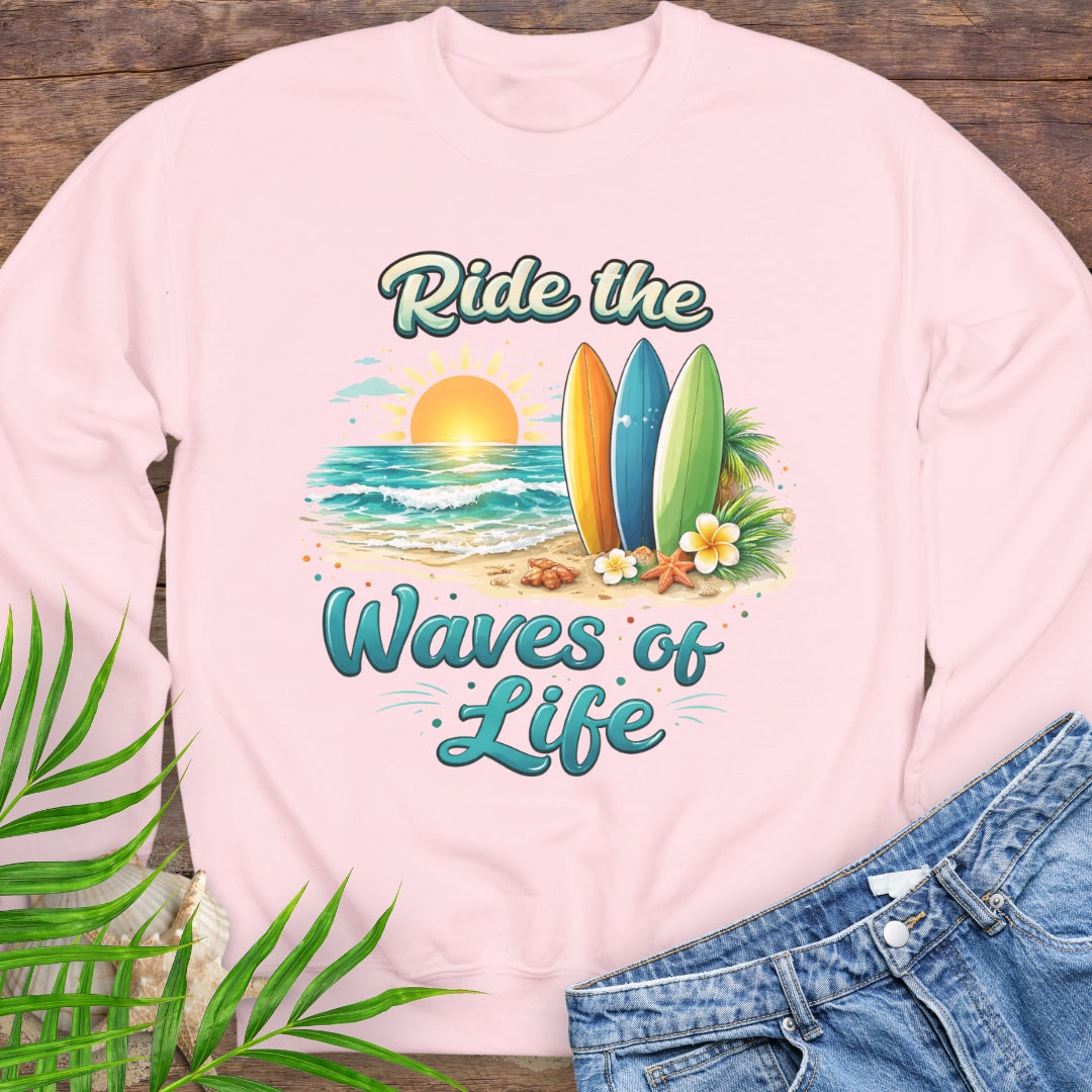 Pink crewneck sweatshirt with inspirational Ride the Waves of Life beach design, showing surfboards, ocean sunset, palm leaves, and sand.