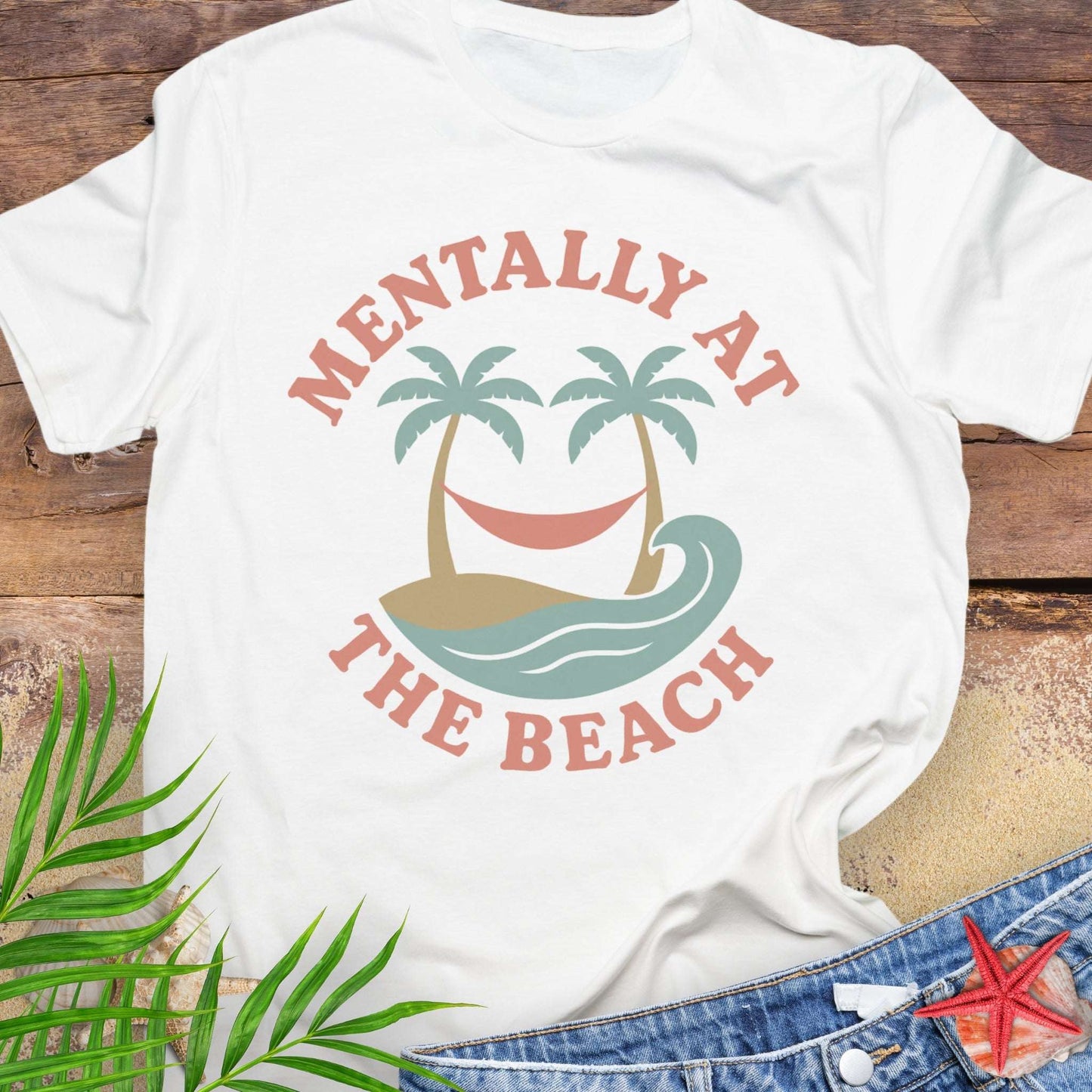 White t-shirt with 'Mentally at the Beach' text with retro design of palm trees with a hammock, and gentle ocean waves.