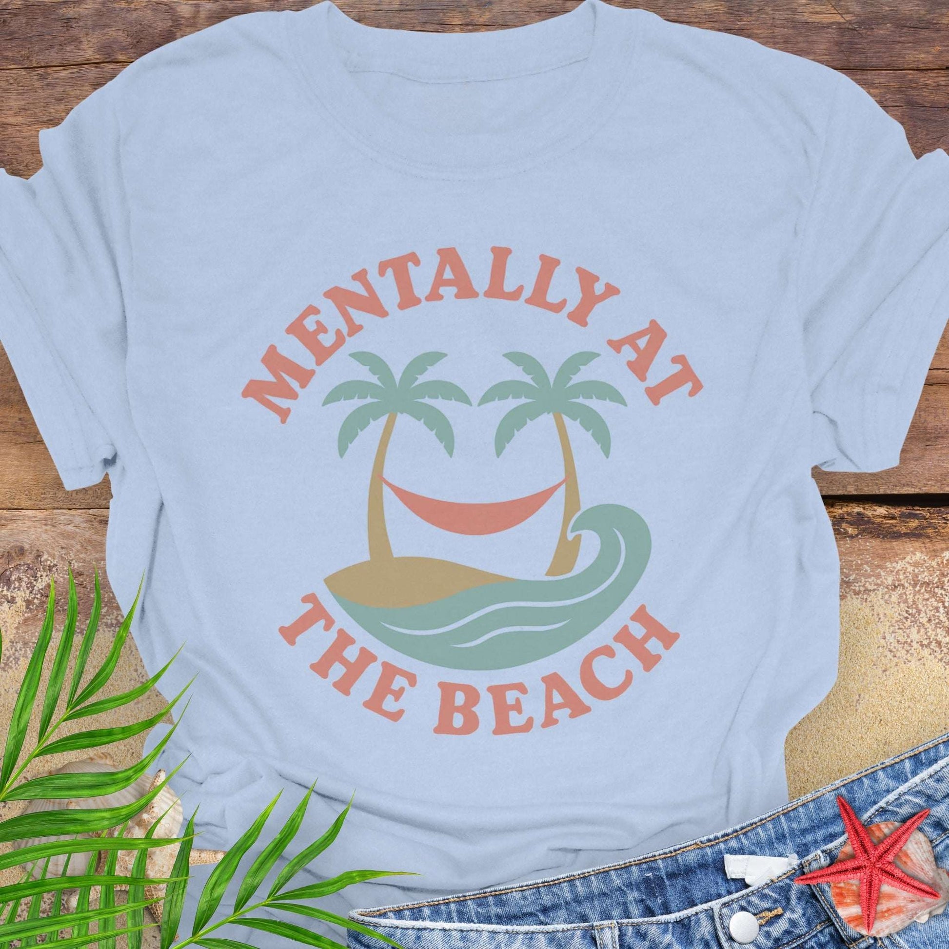 Light blue t-shirt with 'Mentally at the Beach' text with retro design of palm trees with a hammock, and gentle ocean waves.