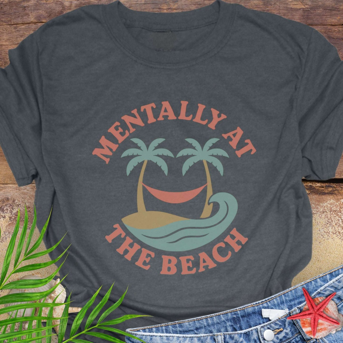 Gray t-shirt with 'Mentally at the Beach' text with retro design of palm trees with a hammock, and gentle ocean waves.