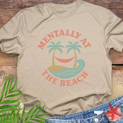Beige t-shirt with 'Mentally at the Beach' text with retro design of palm trees with a hammock, and gentle ocean waves.
