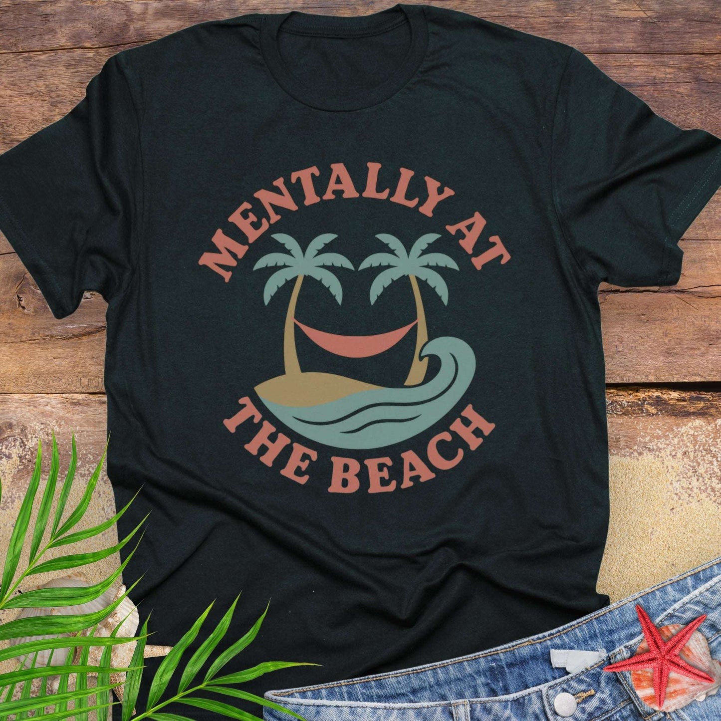 Black t-shirt with 'Mentally at the Beach' text with retro design of palm trees with a hammock, and gentle ocean waves.