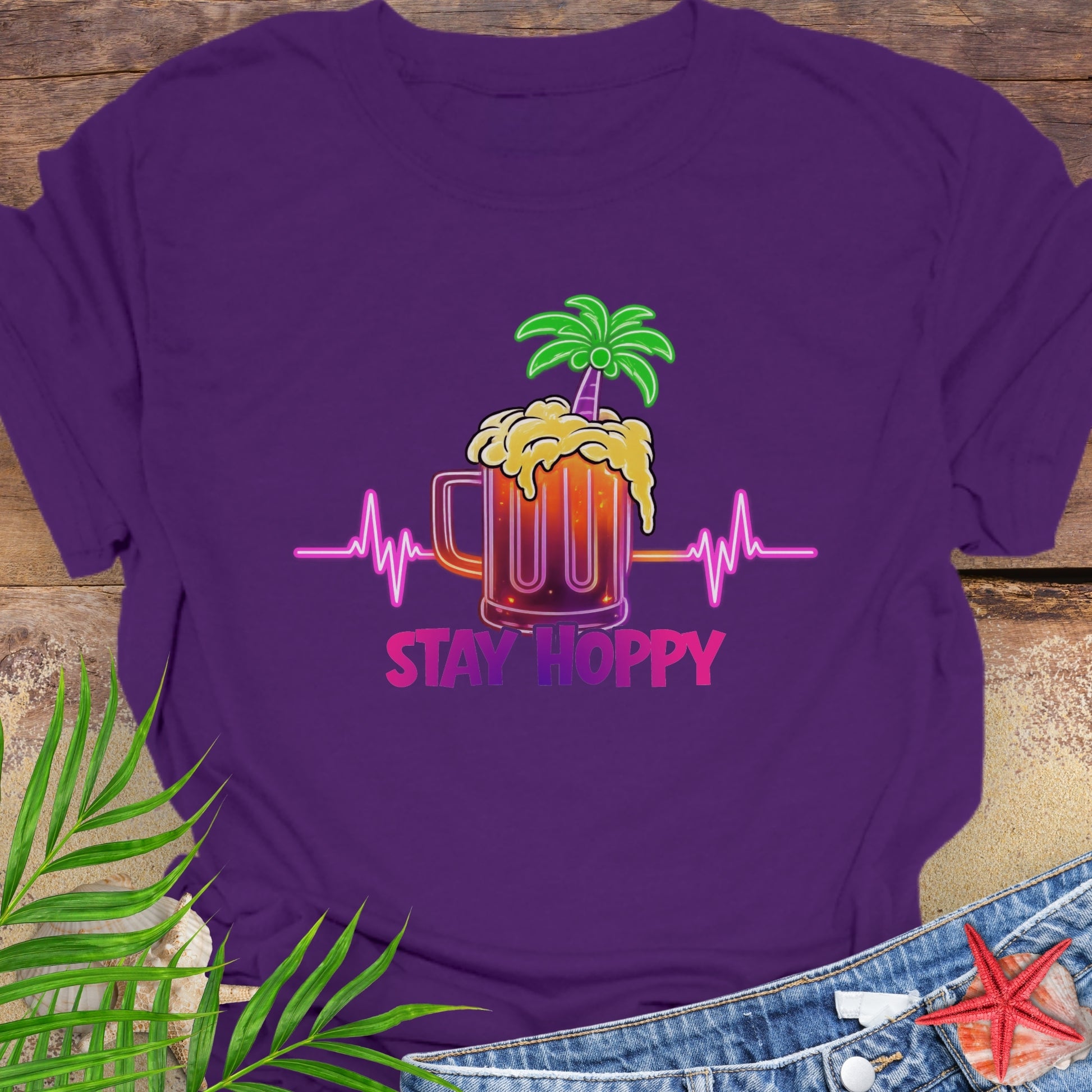 Purple unisex t-shirt with a neon-style graphic of a beer mug, palm tree, and heartbeat line, featuring the phrase “Stay Hoppy” in bold pink and purple.