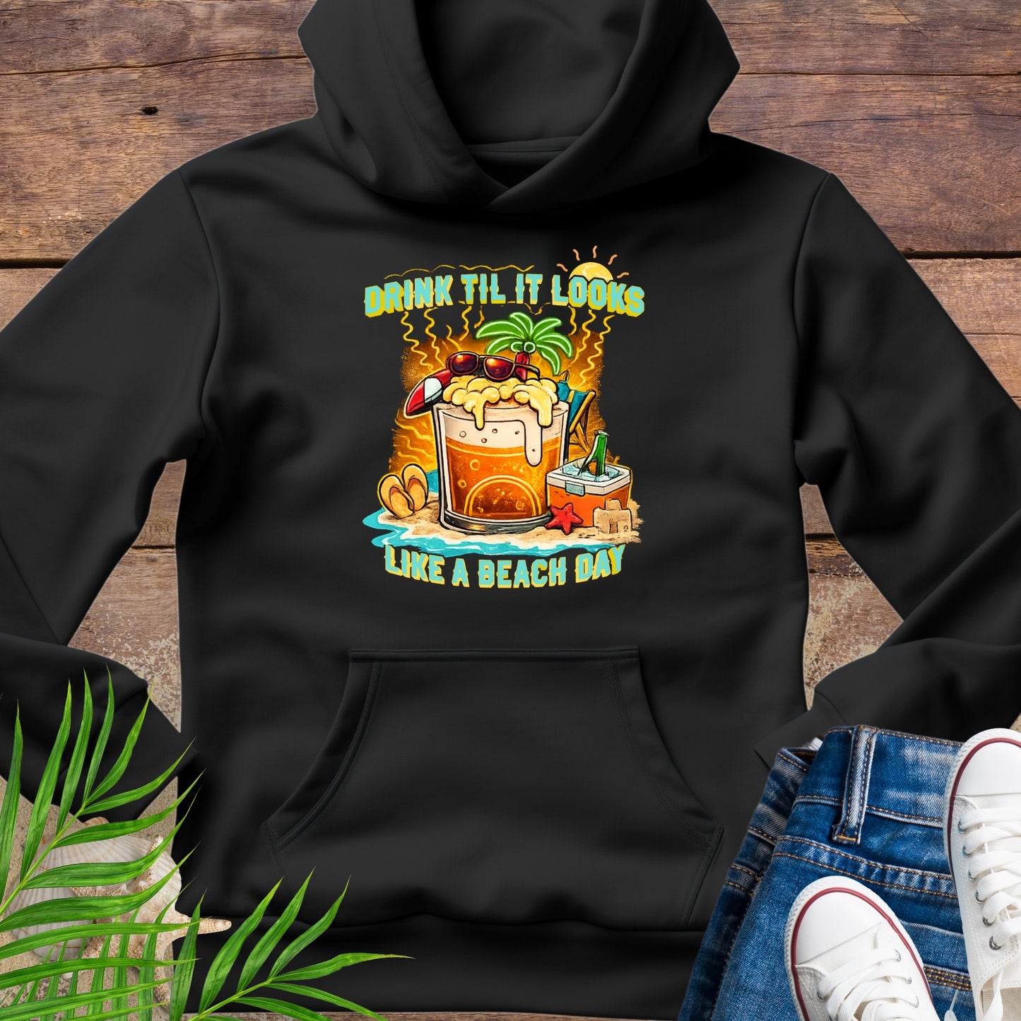 Black pullover hoodie with a tropical cartoon beer mug, palm tree, sunglasses, and the text “Drink Til It Looks Like a Beach Day” in vibrant summer colors.