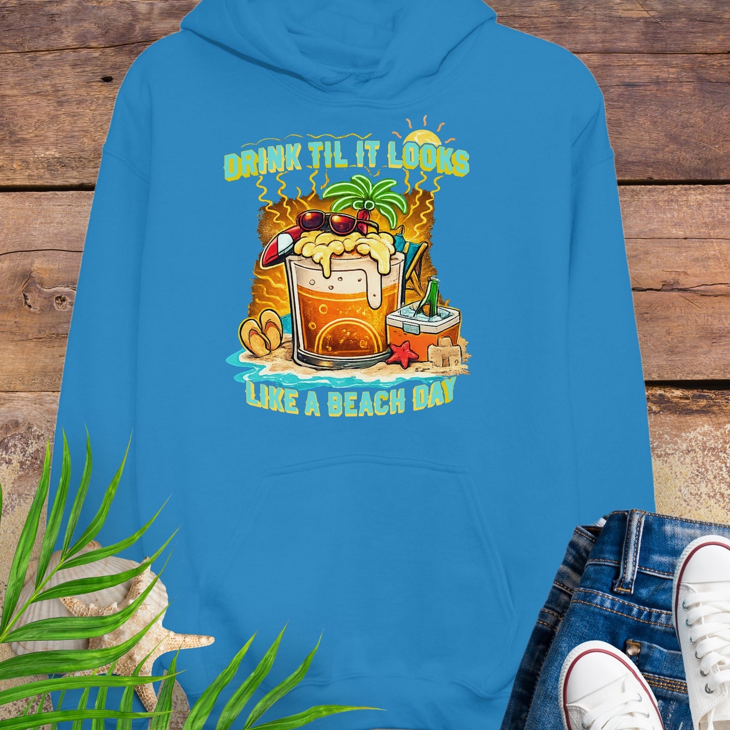 Sapphire Blue pullover hoodie with a tropical cartoon beer mug, palm tree, sunglasses, and the text “Drink Til It Looks Like a Beach Day” in vibrant summer colors.
