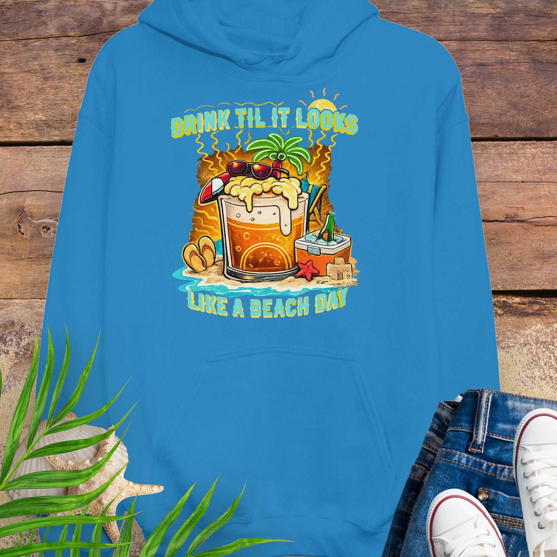 Sapphire Blue pullover hoodie with a tropical cartoon beer mug, palm tree, sunglasses, and the text “Drink Til It Looks Like a Beach Day” in vibrant summer colors.