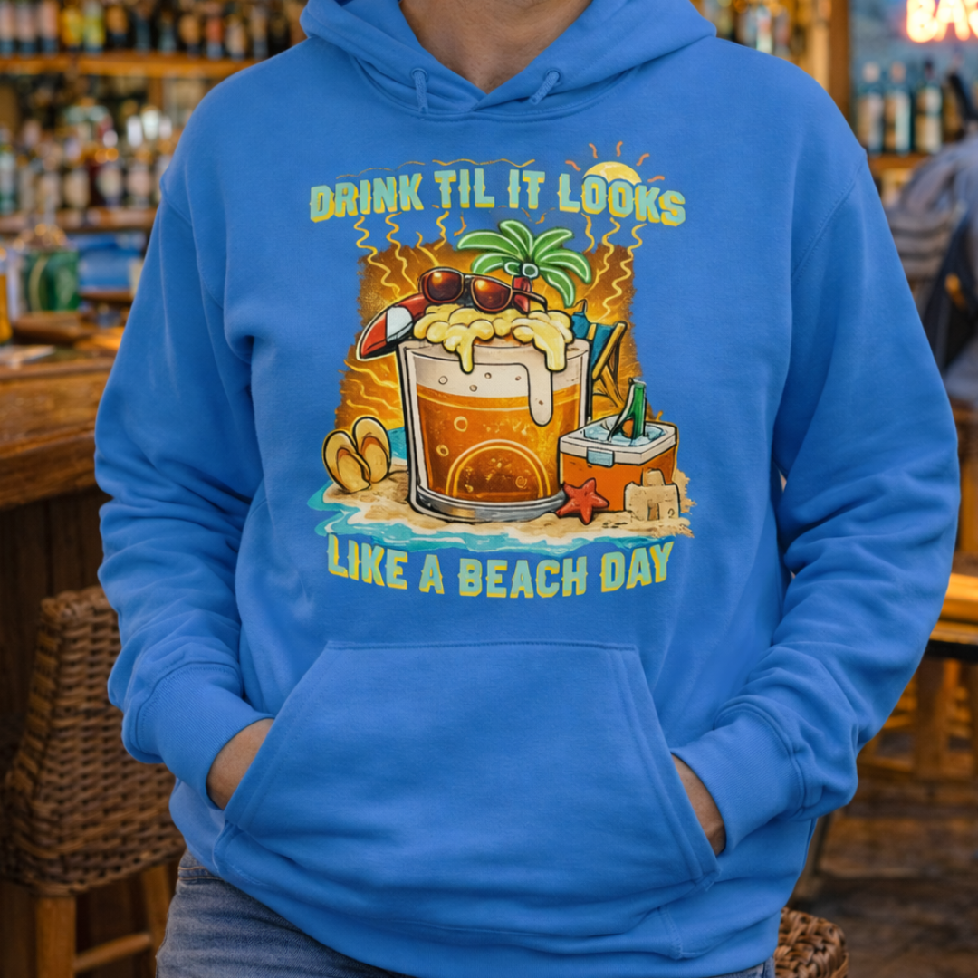 Man wearing a blue pullover hoodie with a tropical cartoon beer mug, palm tree, sunglasses, and the text “Drink Til It Looks Like a Beach Day” in vibrant summer colors.