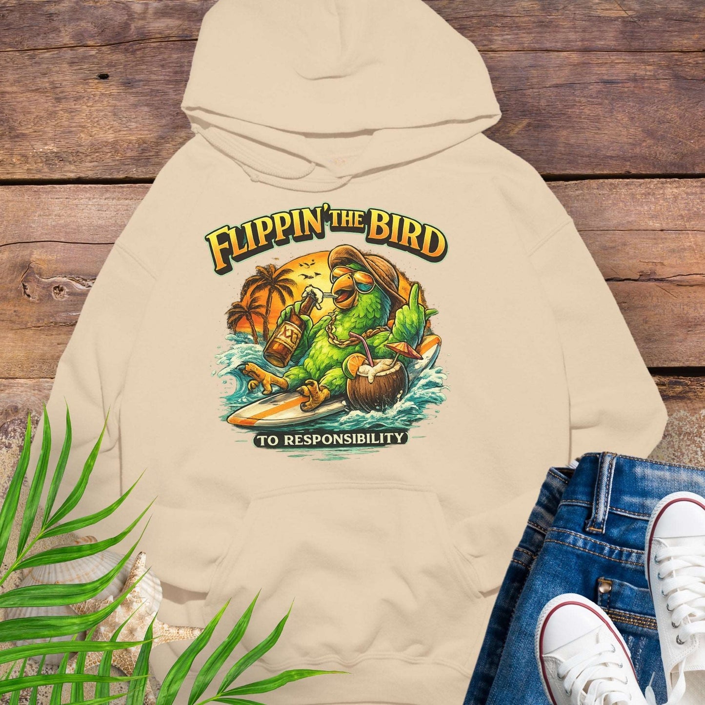 Beige tropical graphic hoodie featuring a green parrot surfing with sunglasses, holding a beer, with coconut drink and sunset palms; text reads “Flippin’ the Bird (to responsibility)”.