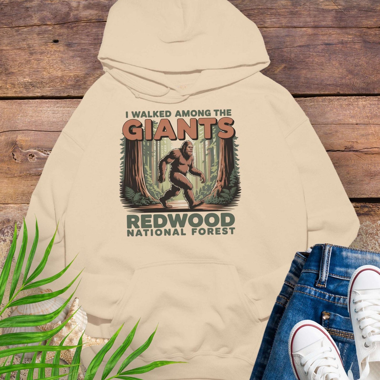 Beige hoodie with 'I Walked Among the Giants' Redwood National Forest design on a wooden background.