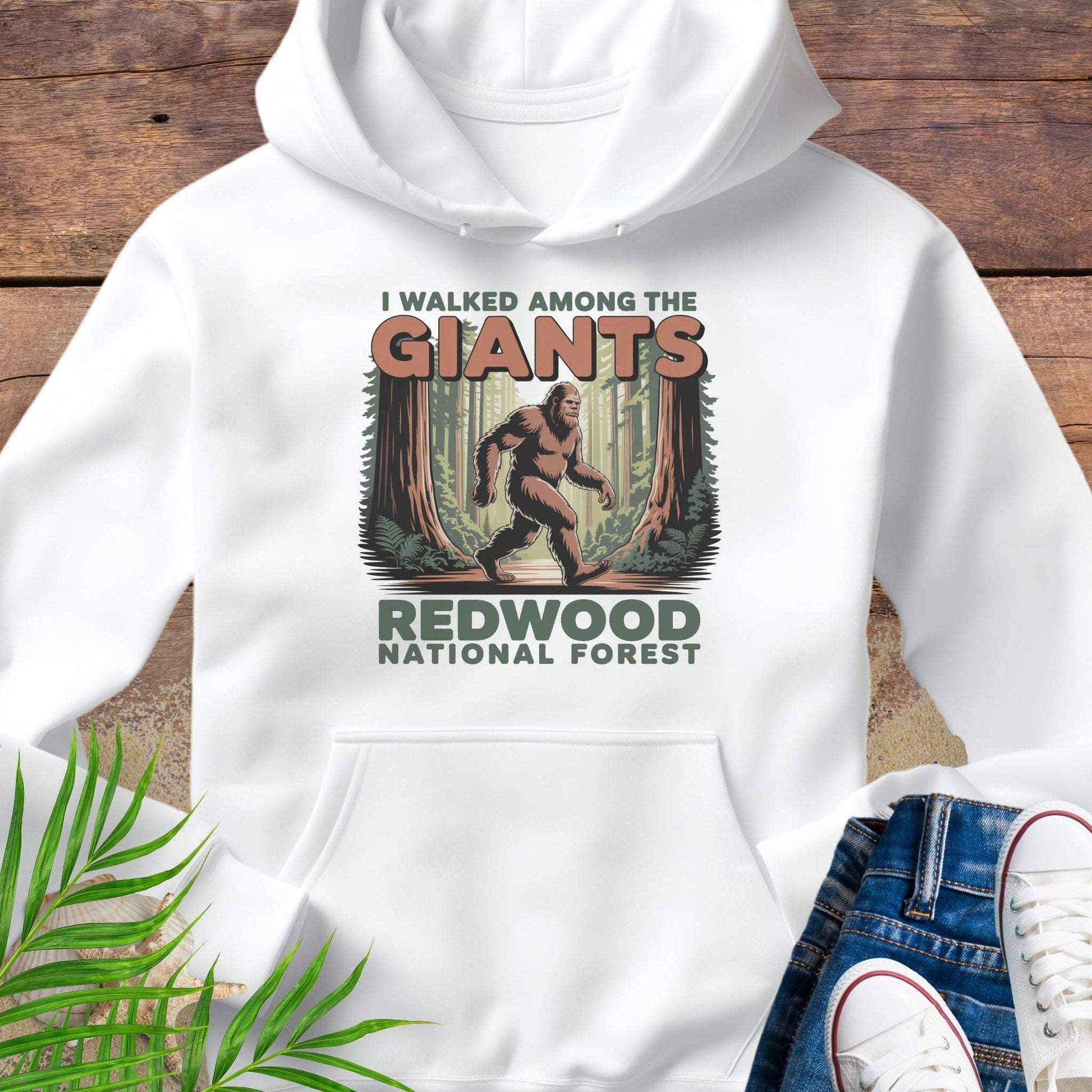 White hoodie with 'I Walked Among the Giants' Redwood National Forest design on a wooden surface.