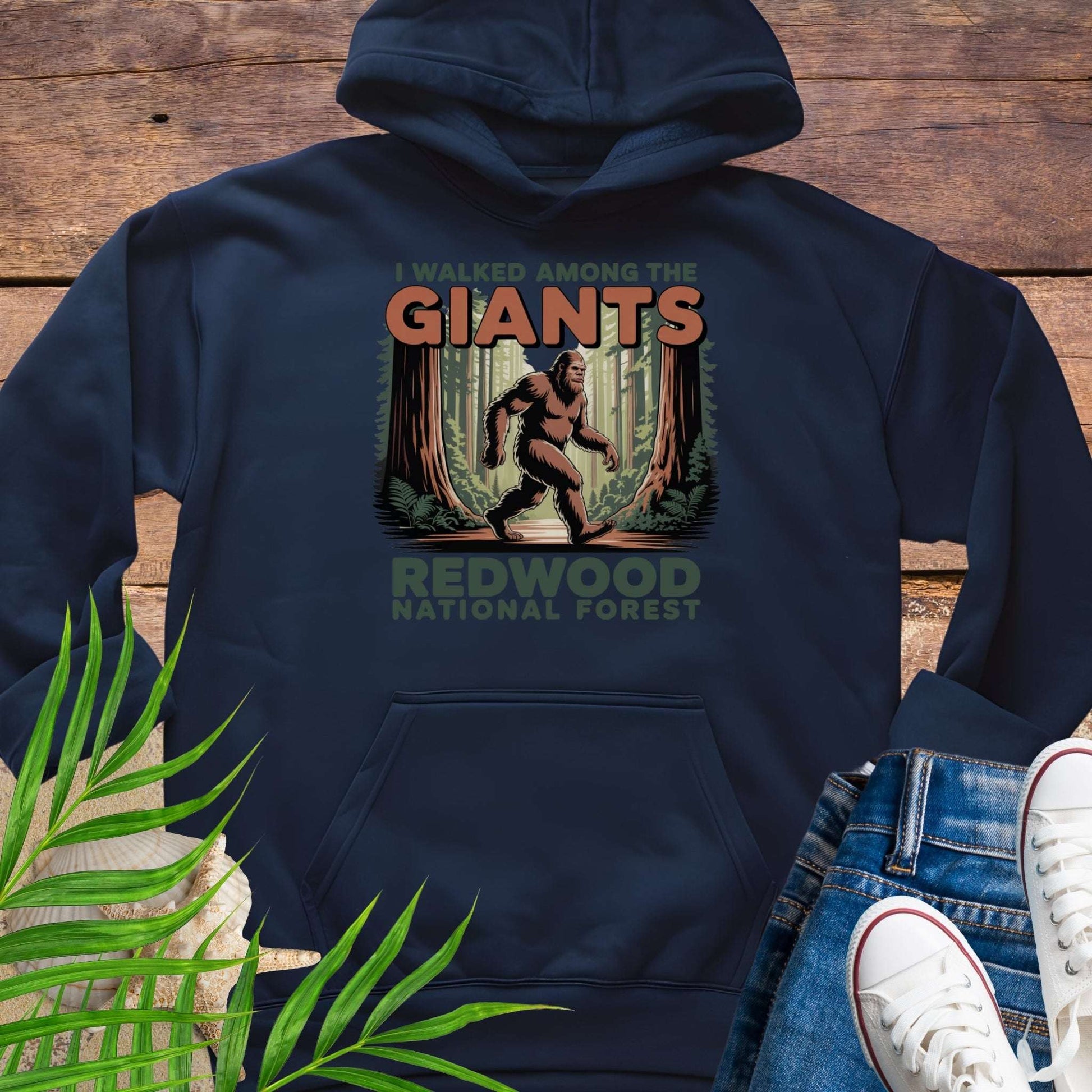 Navy hoodie with 'I Walked Among the Giants' design featuring a Sasquatch in a forest, on a wooden background.