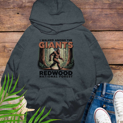 Gray hoodie with 'I Walked Among the Giants' design on a wooden surface with jeans and sneakers.