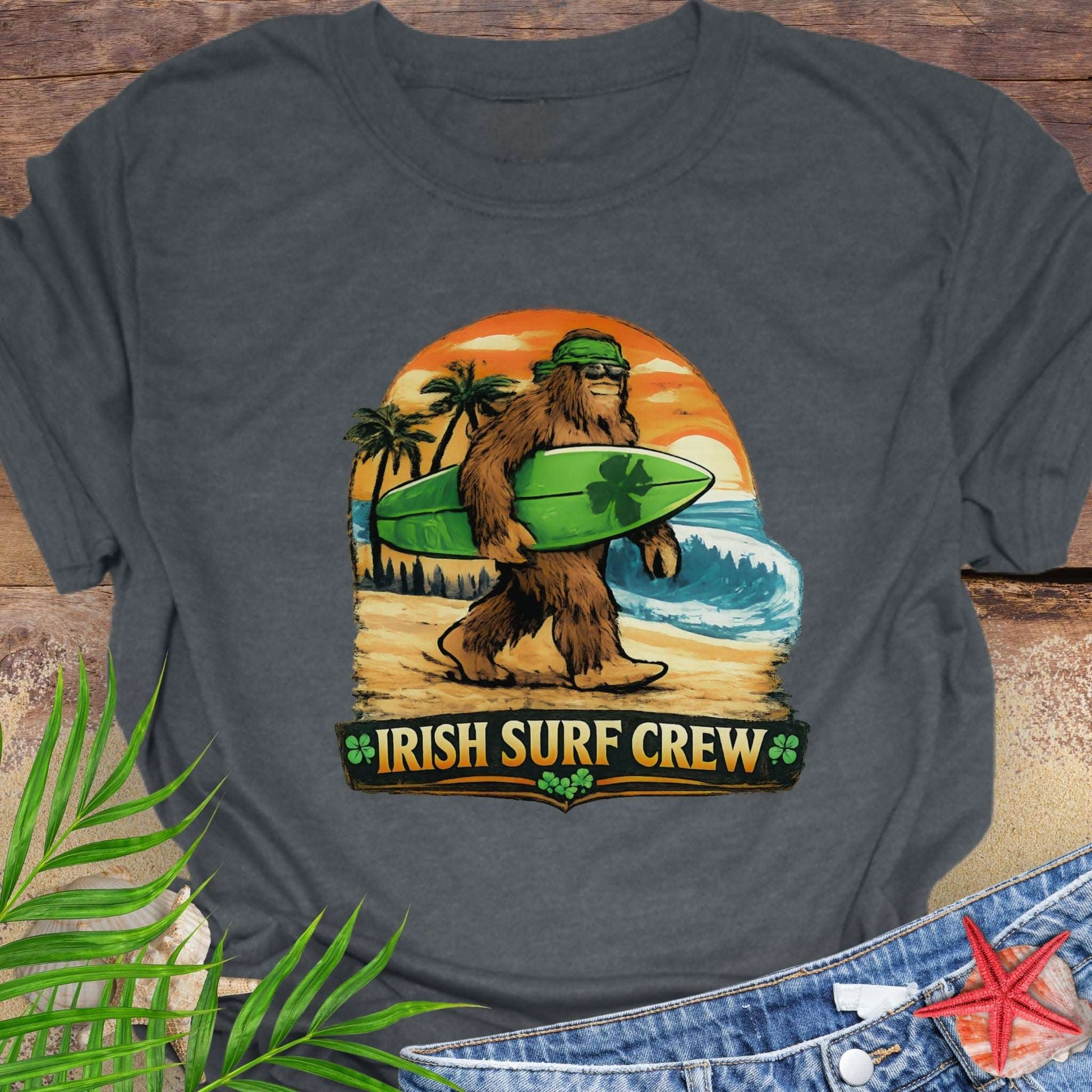 Gray t-shirt with Bigfoot carrying a shamrock-decorated surfboard at the beach, with text “Irish Surf Crew”