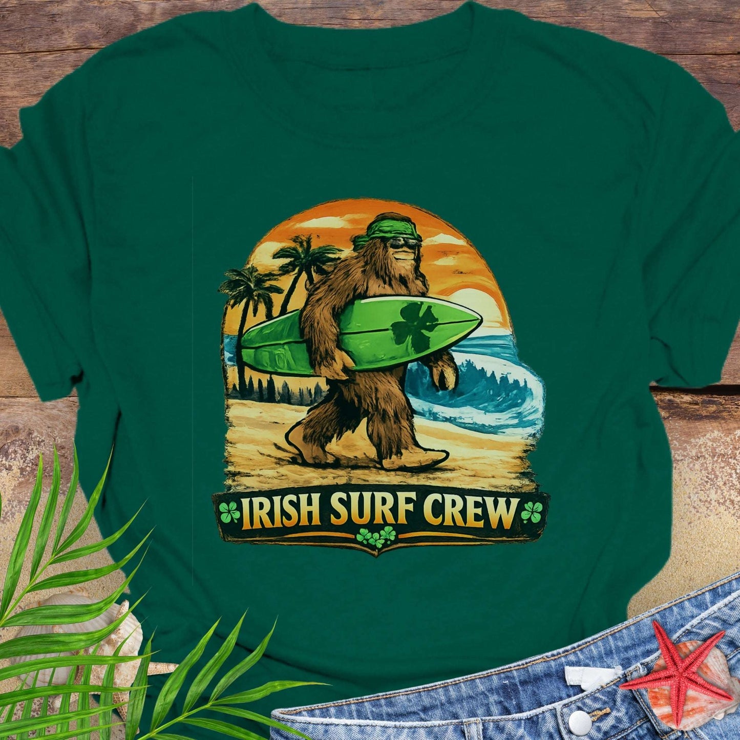 Green t-shirt with Bigfoot carrying a shamrock-decorated surfboard at the beach, with text “Irish Surf Crew”