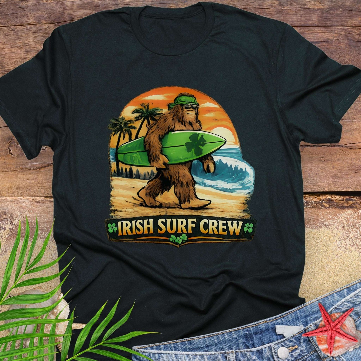 Black t-shirt with Bigfoot carrying a shamrock-decorated surfboard at the beach, with text “Irish Surf Crew”