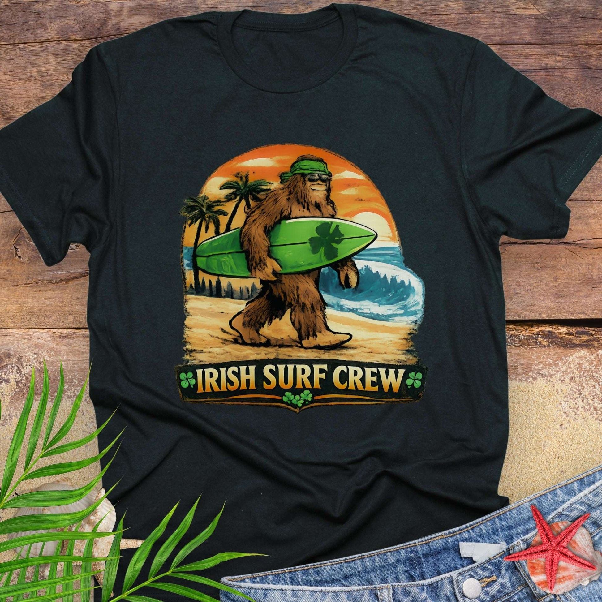 Black t-shirt with Bigfoot carrying a shamrock-decorated surfboard at the beach, with text “Irish Surf Crew”