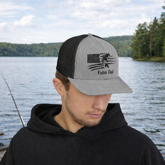 Man wearing an embroidered cap with 'Fishing Dad' text by a lake.