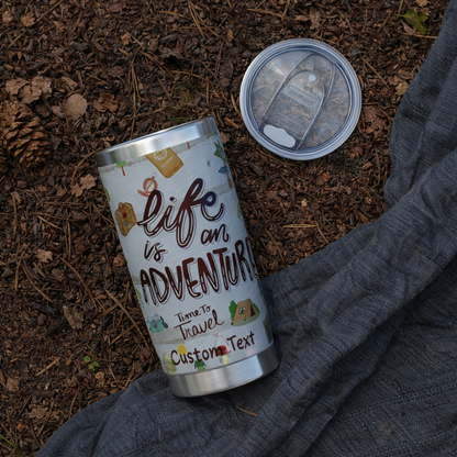 Silver tumbler with 'Life is an Adventure' text on a natural background