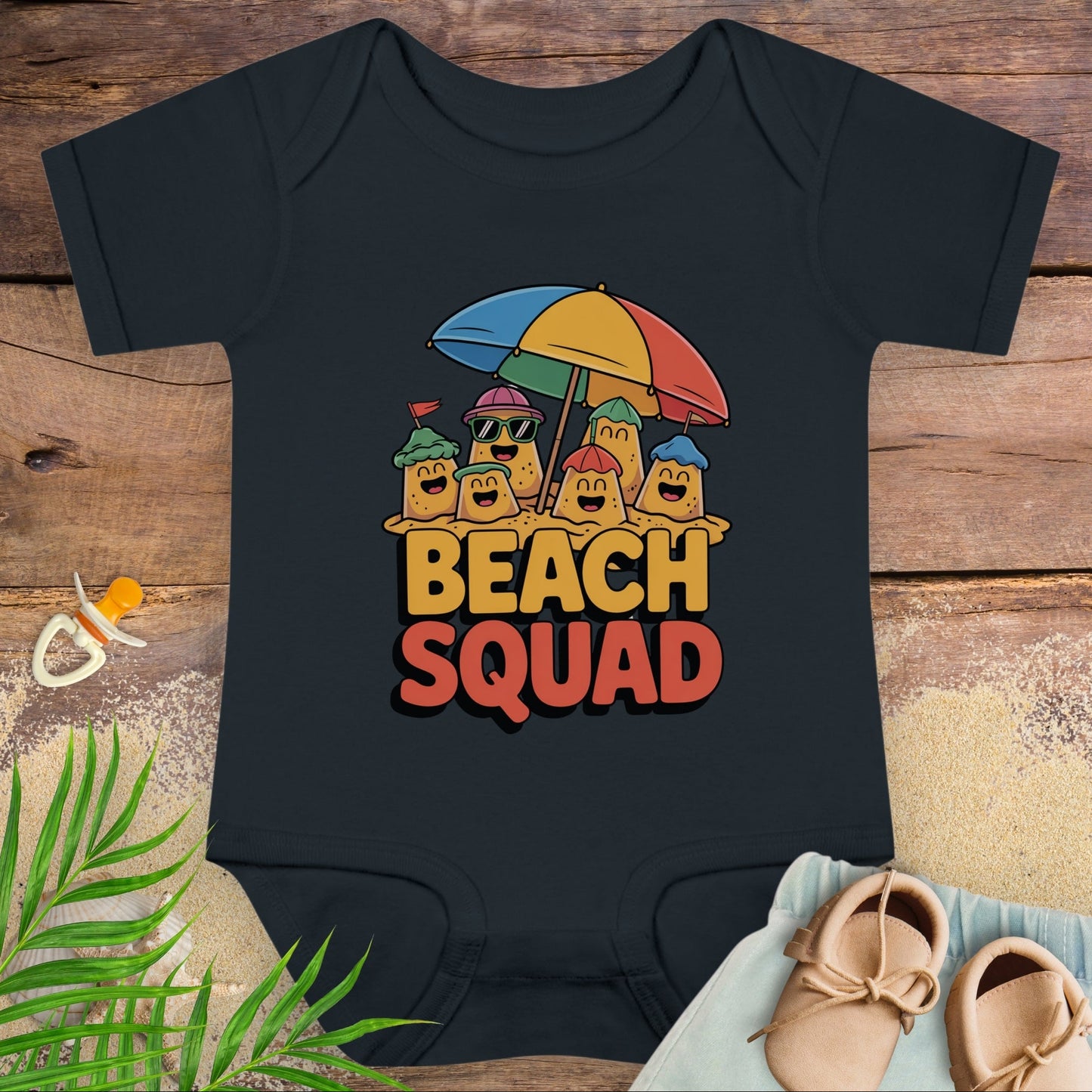 Black baby onesie with 'Beach Squad' design on a wooden surface with a pacifier and shoes.