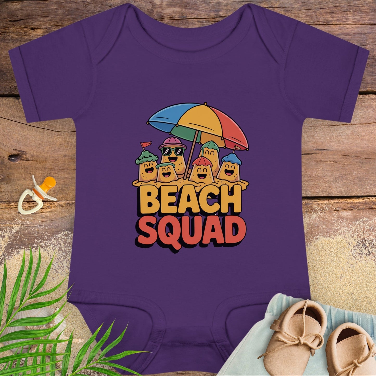 Purple baby onesie with 'Beach Squad' design on a wooden surface with beach-themed items.